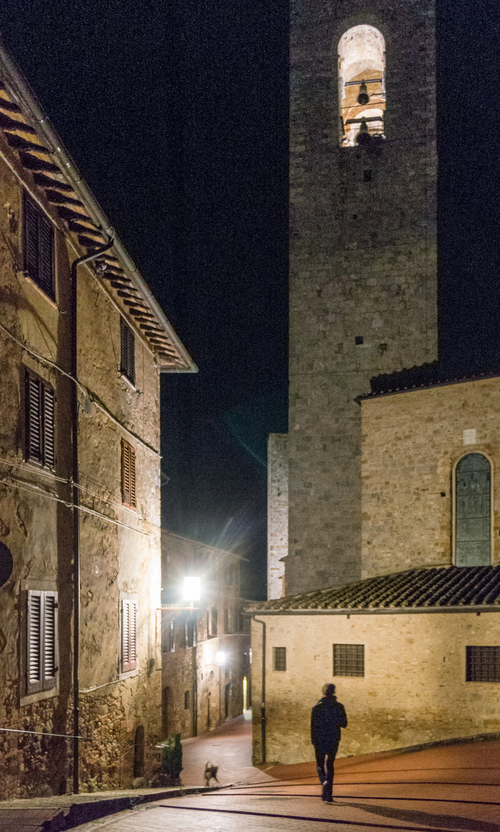 A person walks with their dog on a deserted street at night in San Gimignano, Italy | Photo by Mike Hudak