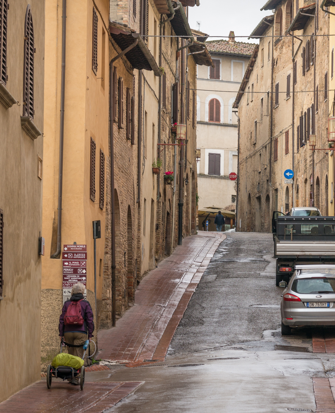 A lone pilgrim on the Via Francigena walks through San Gimignano, Italy, on a rainy day | Photo by Mike Hudak